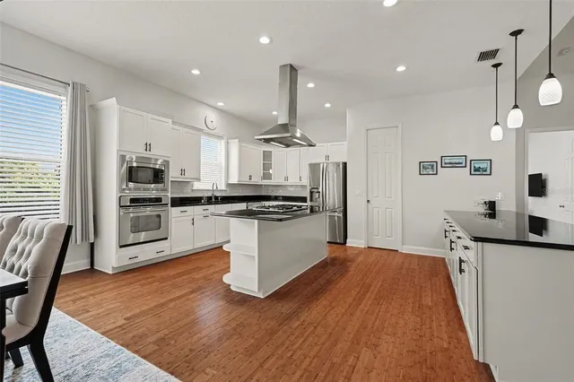 a kitchen with stainless steel appliances kitchen island granite countertop a refrigerator a stove top oven a sink dishwasher and white cabinets with wooden floor