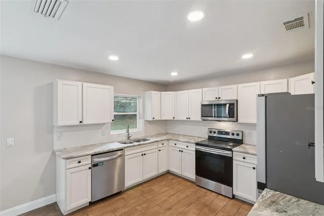 a large kitchen with stainless steel appliances granite countertop a stove top oven a refrigerator a sink and dishwasher with white cabinets