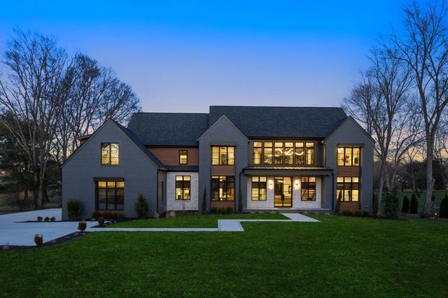 a view of a brick house next to a yard with a large tree