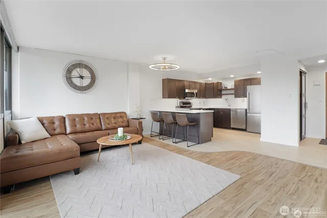 a living room with stainless steel appliances furniture a rug and a kitchen view