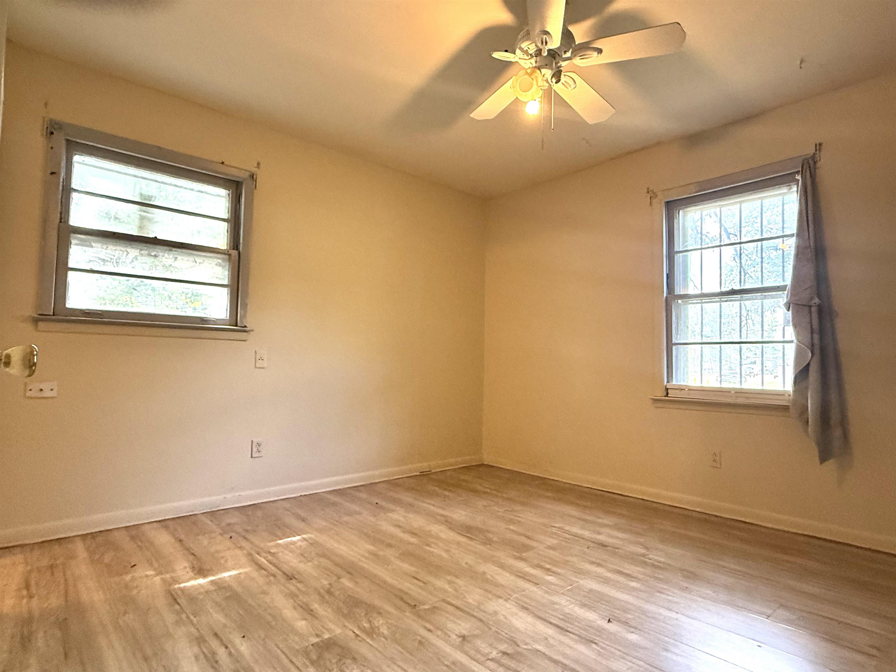 2930 Getwell Road Memphis, TN 38118 - Photo 8 of 25 Room featuring wood-finish flooring, two windows with security bars, a ceiling fan with light fixture, and neutral-toned walls