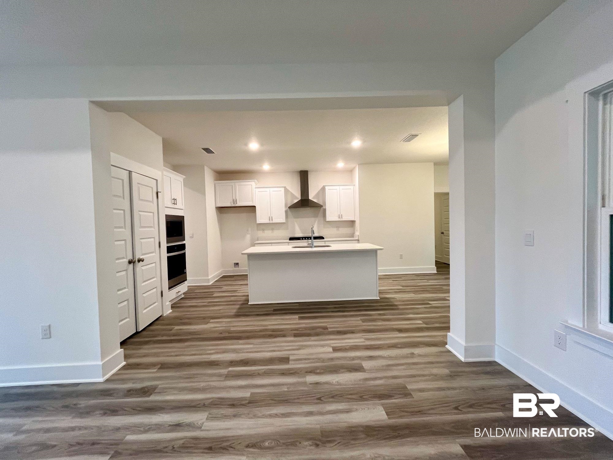 334 Barndling Street Fairhope, AL 36532 - Photo 12 of 34 Kitchen with white cabinets, a center island with sink, wall chimney range hood, and dark hardwood / wood-style floors