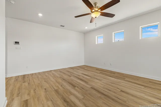an empty room with wooden floor and a ceiling fan