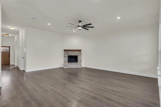an empty room with wooden floor a ceiling fan a kitchen view and a fireplace