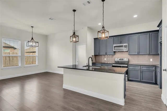 a kitchen with stainless steel appliances granite countertop a sink a stove a refrigerator and a wooden floor