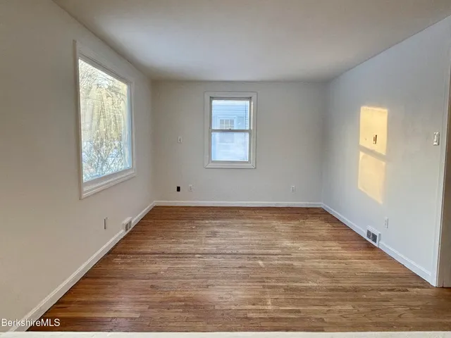a view of an empty room with wooden floor and window