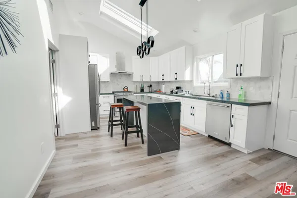 a kitchen with stainless steel appliances granite countertop a refrigerator a sink dishwasher a stove top oven a dining table and chairs with wooden floor