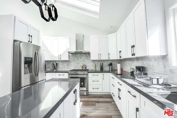 a kitchen with stainless steel appliances granite countertop a sink a stove a refrigerator and white cabinets