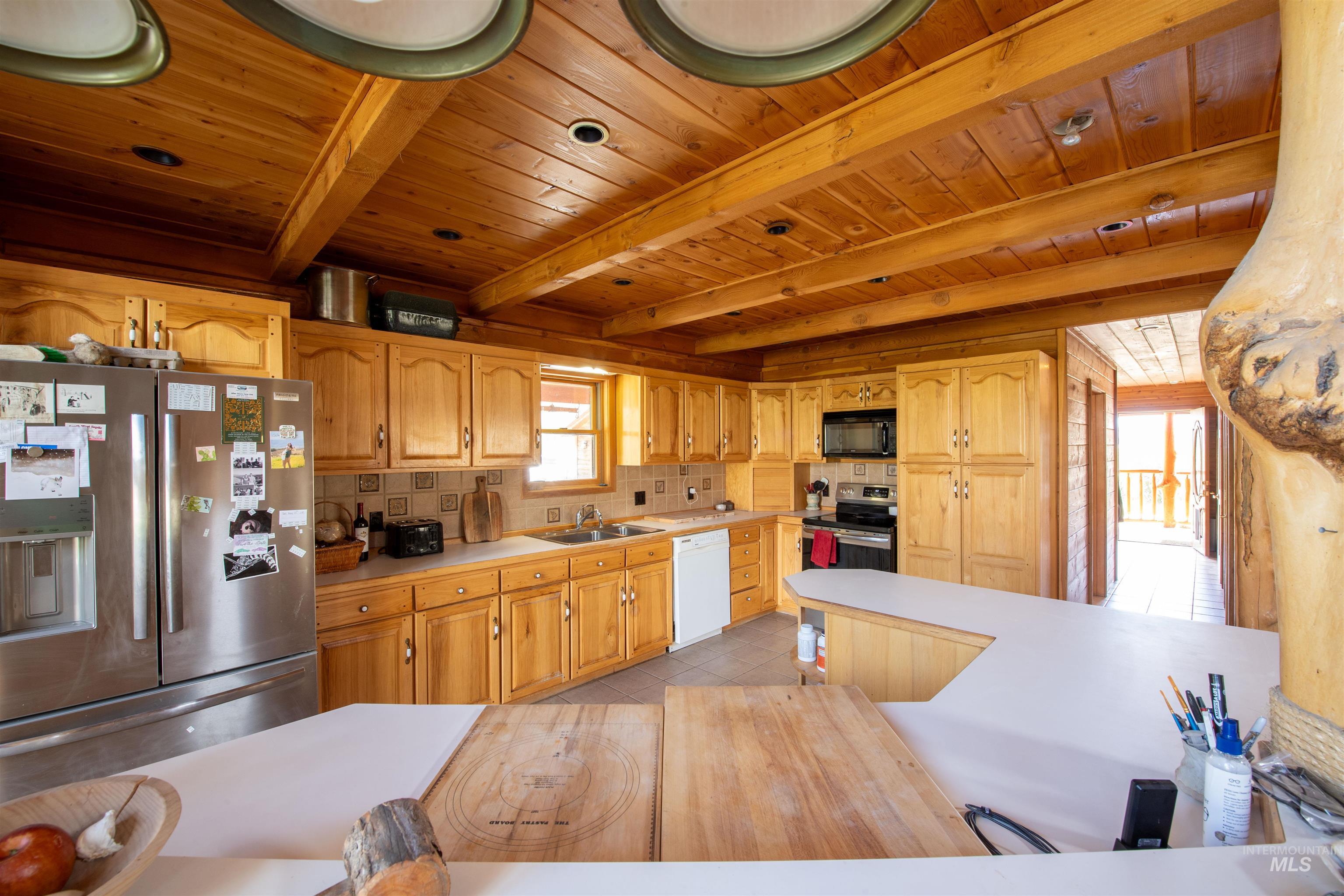 9885 Challis Creek Road Challis, ID 83226 - Photo 12 of 48 Kitchen featuring light countertops, stainless steel appliances, backsplash, a wood ceiling with exposed beams, and light tile patterned floors