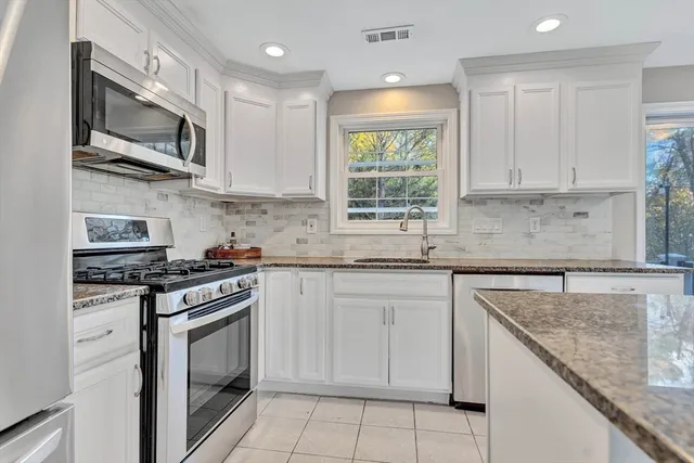 a kitchen with stainless steel appliances granite countertop white cabinets granite counter tops and a window