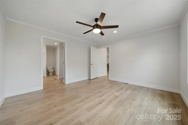 a view of an empty room with wooden floor and a ceiling fan