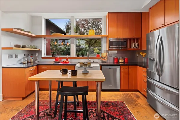 a kitchen with stainless steel appliances granite countertop a stove a refrigerator a sink a dining table and chairs with wooden floor