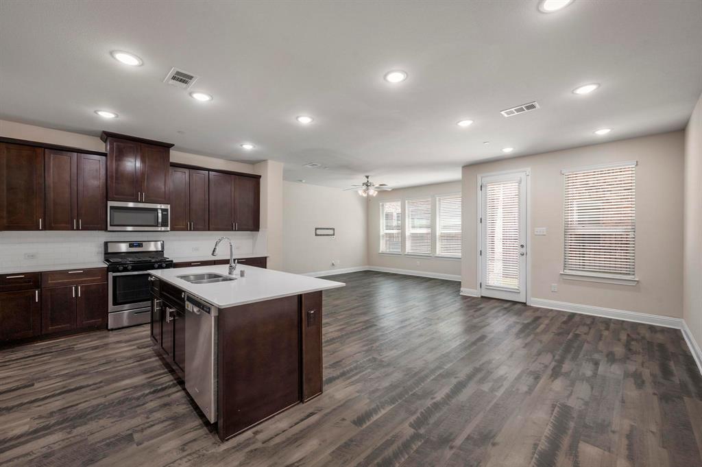 a kitchen with stainless steel appliances granite countertop a stove a sink a refrigerator white cabinets and wooden floor