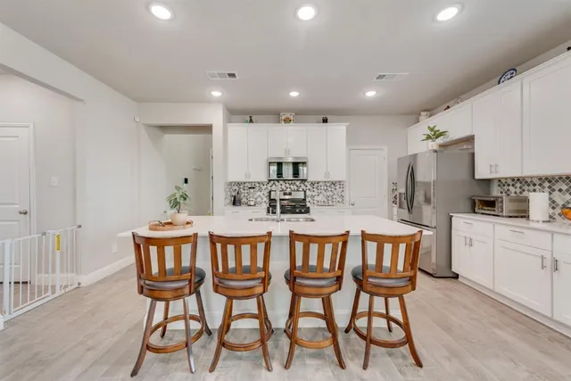 a kitchen with stainless steel appliances kitchen island granite countertop a dining table chairs and white cabinets