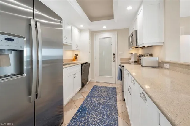 a kitchen with stainless steel appliances granite countertop a refrigerator a sink and white cabinets
