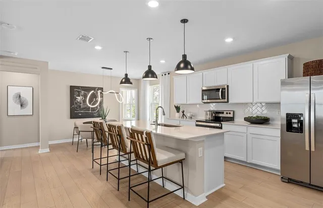 a kitchen with stainless steel appliances kitchen island granite countertop a refrigerator a stove a sink a dining table and chairs with wooden floor