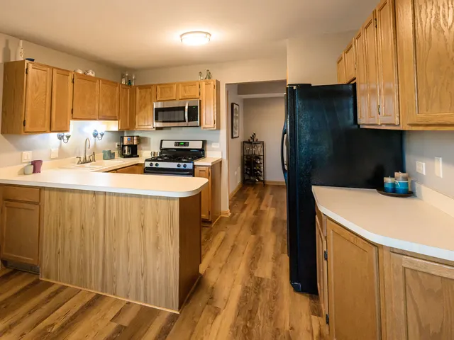 a kitchen with stainless steel appliances a stove a sink a refrigerator white cabinets and wooden floor