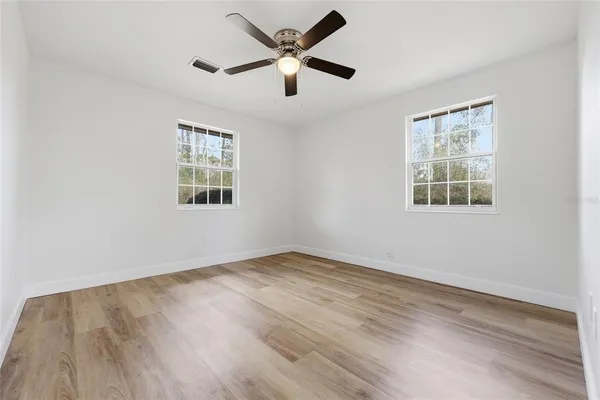 an empty room with wooden floor ceiling fan and windows