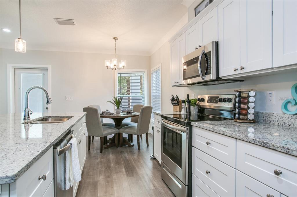 3040 Belcher Road Dunedin, FL 34698 - Photo 10 of 24 a kitchen with stainless steel appliances granite countertop a sink dishwasher stove and white cabinets with wooden floor