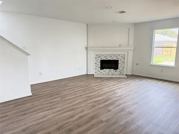 an empty room with wooden floor fireplace and windows