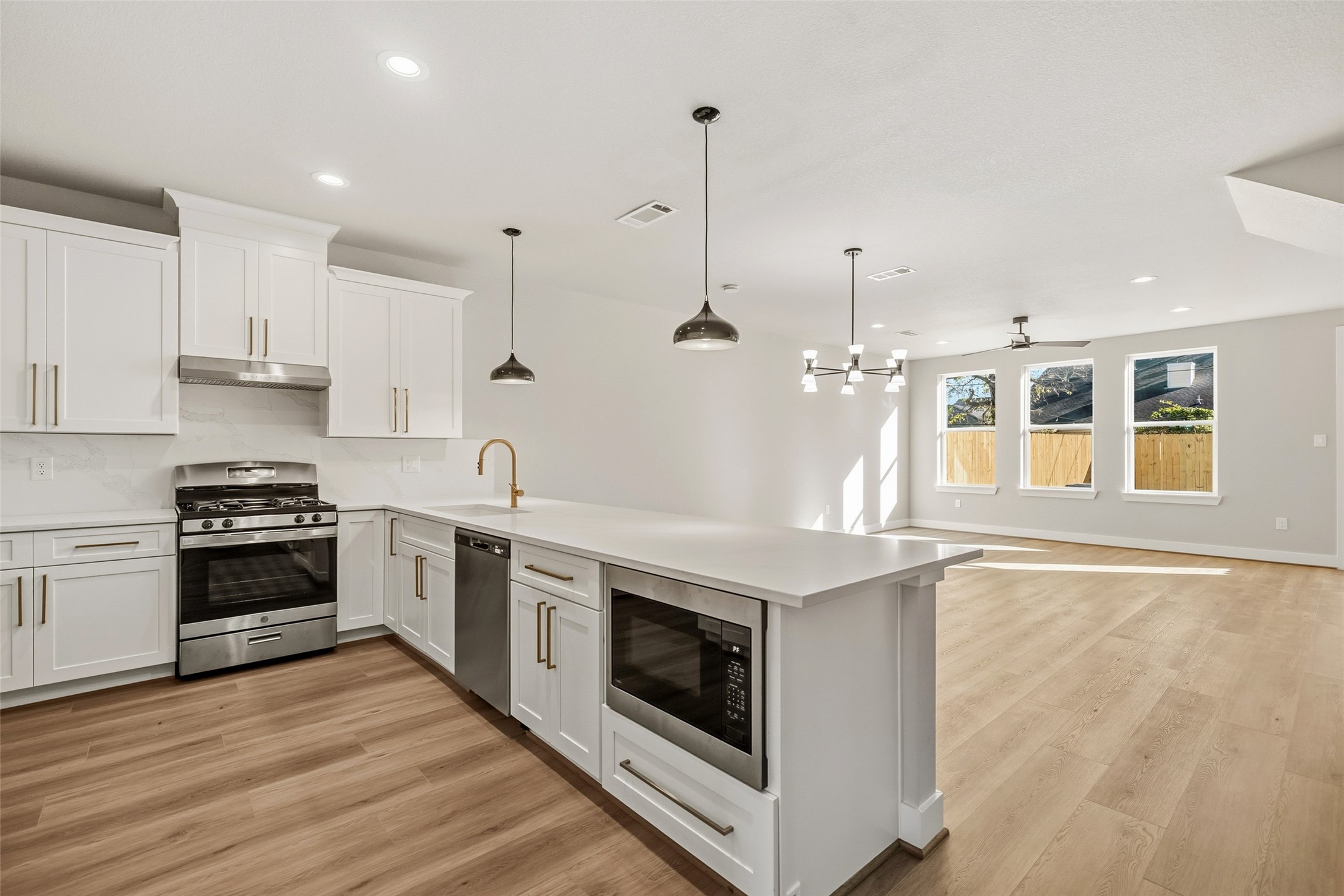 3422 Elser Street Houston, TX 77009 - Photo 8 of 26 This photo showcases a spacious, modern open-concept kitchen and living area. The kitchen features sleek white cabinetry, stainless steel appliances, and a large island with pendant lighting. The living area has ample natural light from large windows and beautiful wood flooring, creating a warm, inviting atmosphere.