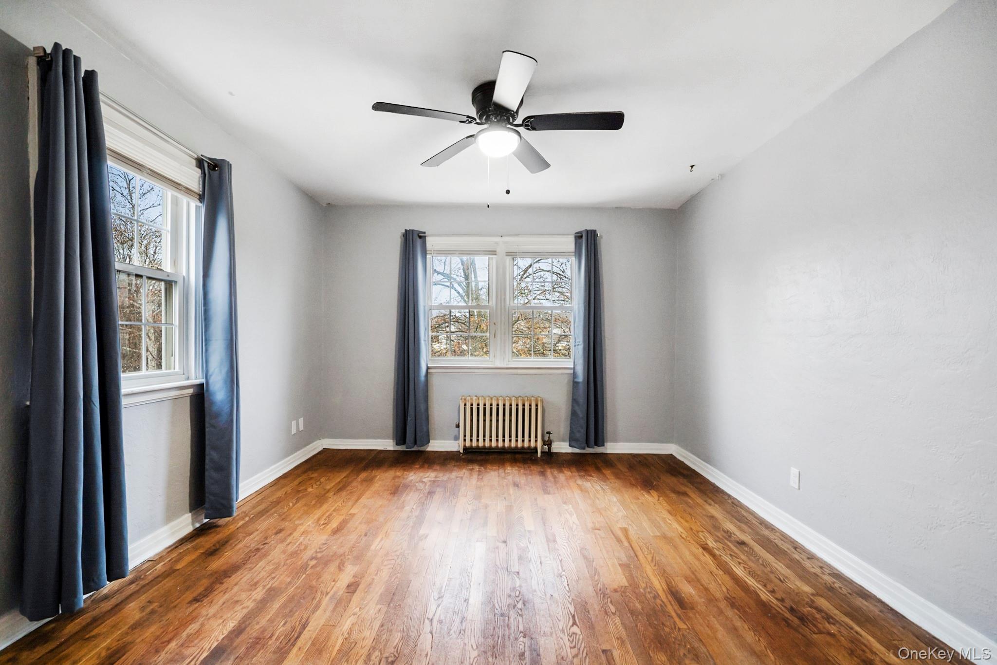 86-33 253rd Street Queens, NY 11426 - Photo 8 of 17 an empty room with wooden floor a ceiling fan and windows