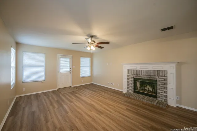 a view of an empty room with wooden floor fireplace and a window