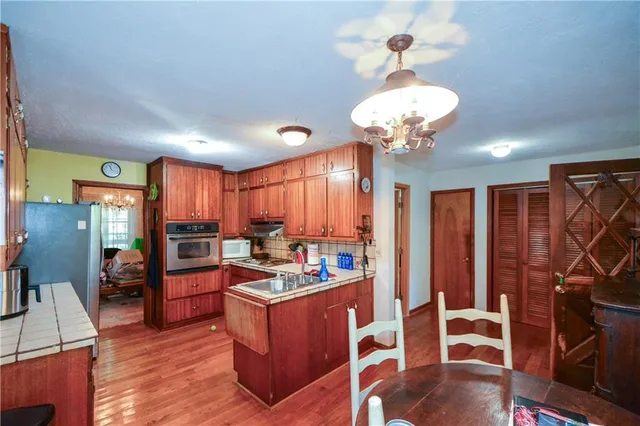 a kitchen with stainless steel appliances granite countertop a refrigerator a sink dishwasher a dining table and chairs with wooden floor