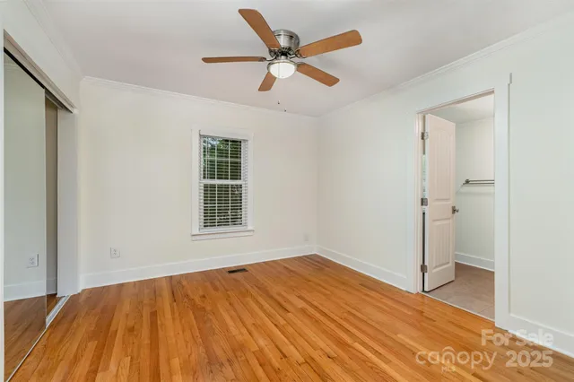 a view of an empty room with wooden floor and a ceiling fan