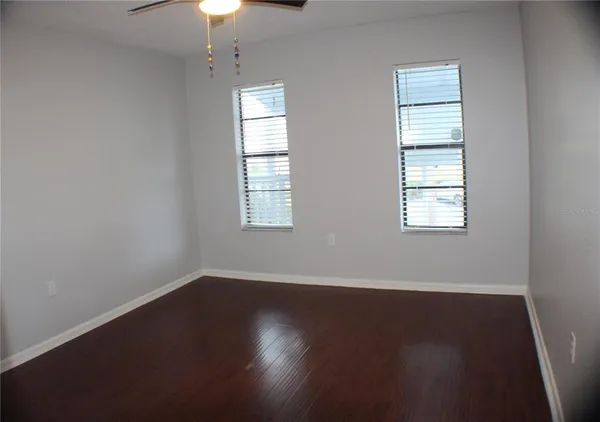 an empty room with wooden floor chandelier fan and windows
