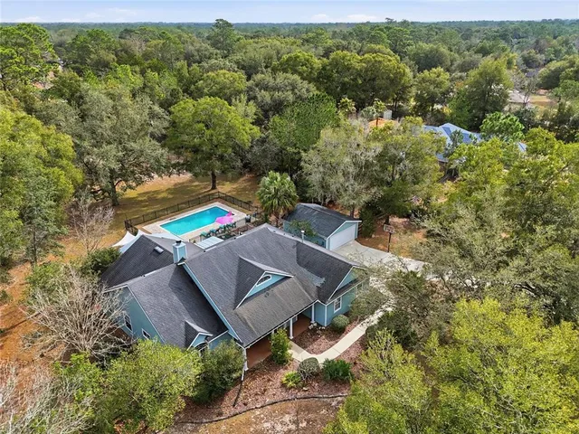 an aerial view of a house with pool big yard and large trees