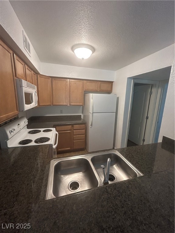 3145 East Flamingo Road, Unit 1014 Las Vegas, NV 89121 - Photo 11 of 17 Kitchen with dark countertops, freestanding refrigerator, range, a textured ceiling, and brown cabinetry