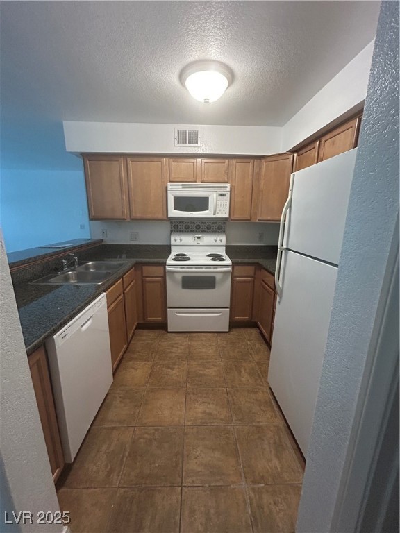 3145 East Flamingo Road, Unit 1014 Las Vegas, NV 89121 - Photo 10 of 17 Kitchen with white appliances, brown cabinets, a textured ceiling, a textured wall, and dark tile patterned flooring