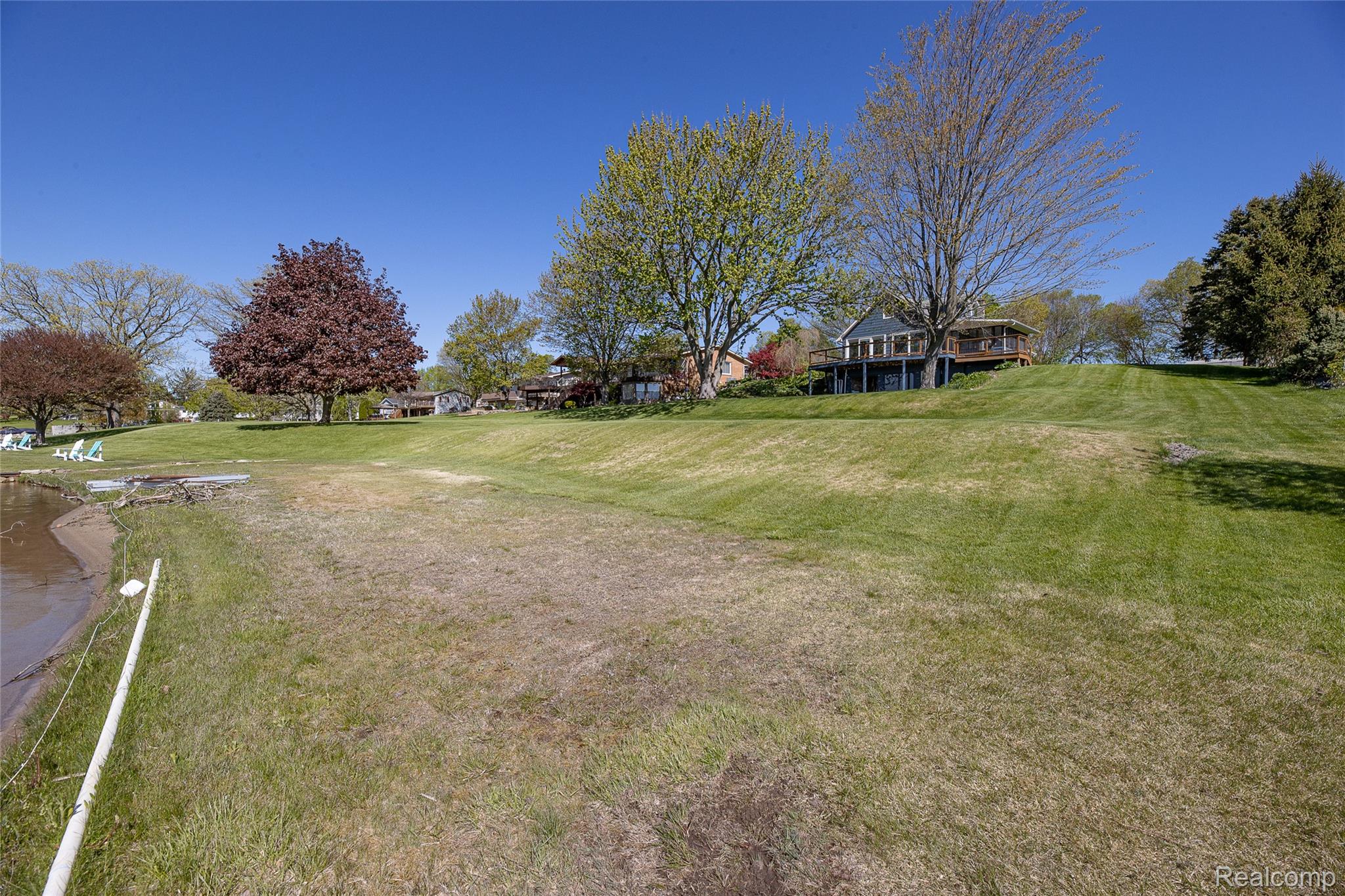 2855 Farmers Creek Road Metamora, MI 48455 - Photo 9 of 51 Expansive grassy terrain bordering a body of water, featuring mature trees and a distant residence with an elevated deck