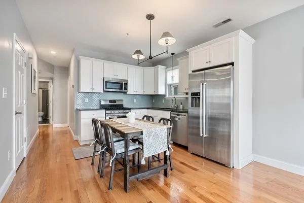 a kitchen with stainless steel appliances granite countertop a refrigerator a stove top oven a sink dishwasher a dining table and chairs with wooden floor