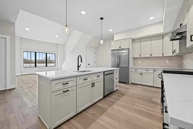 a large white kitchen with cabinets a sink a window and stainless steel appliances