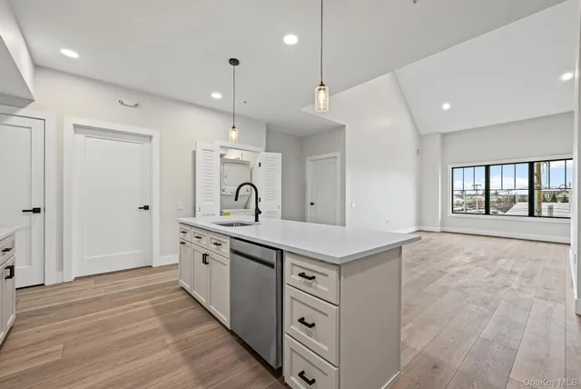 a large kitchen with stainless steel appliances granite countertop a stove a sink a refrigerator and white cabinets with wooden floor