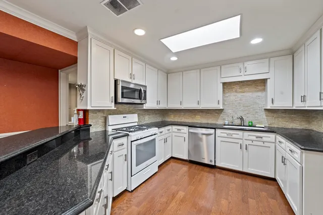 a kitchen with stainless steel appliances granite countertop a stove top oven a sink and dishwasher a refrigerator with wooden floor