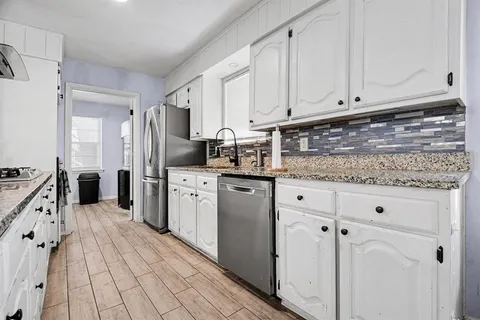 a kitchen with granite countertop a sink stainless steel appliances and white cabinets