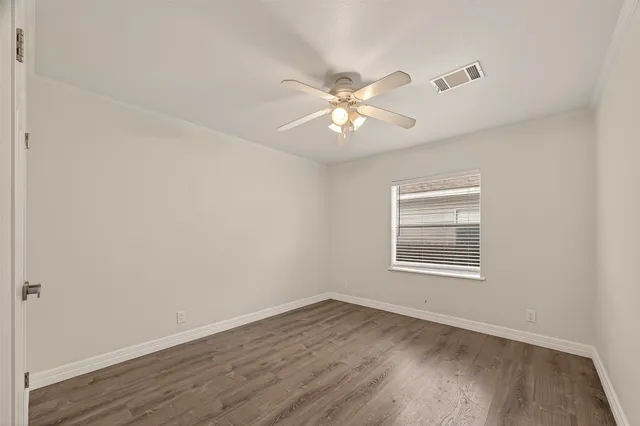 an empty room with wooden floor fan and windows