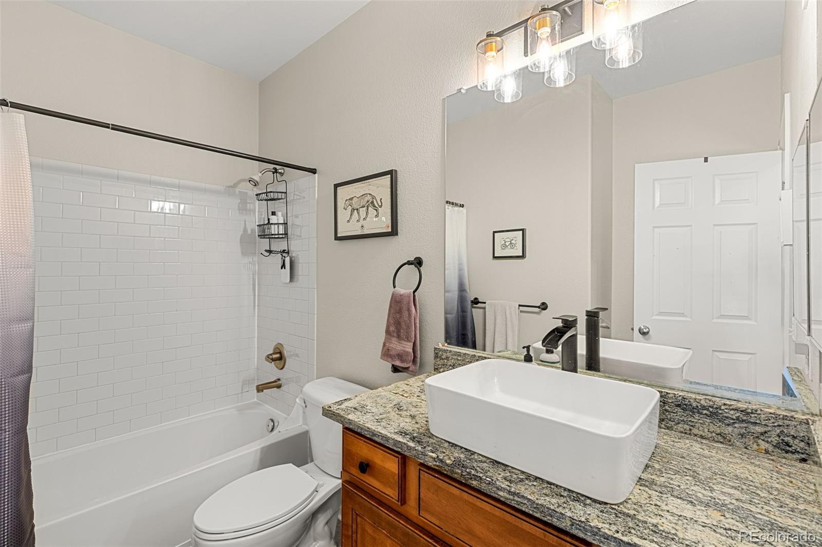 8073 West 51st Place, Unit 303 Arvada, CO 80002 - Photo 36 of 48 a bathroom with a granite countertop sink a toilet a mirror a bathtub and shower