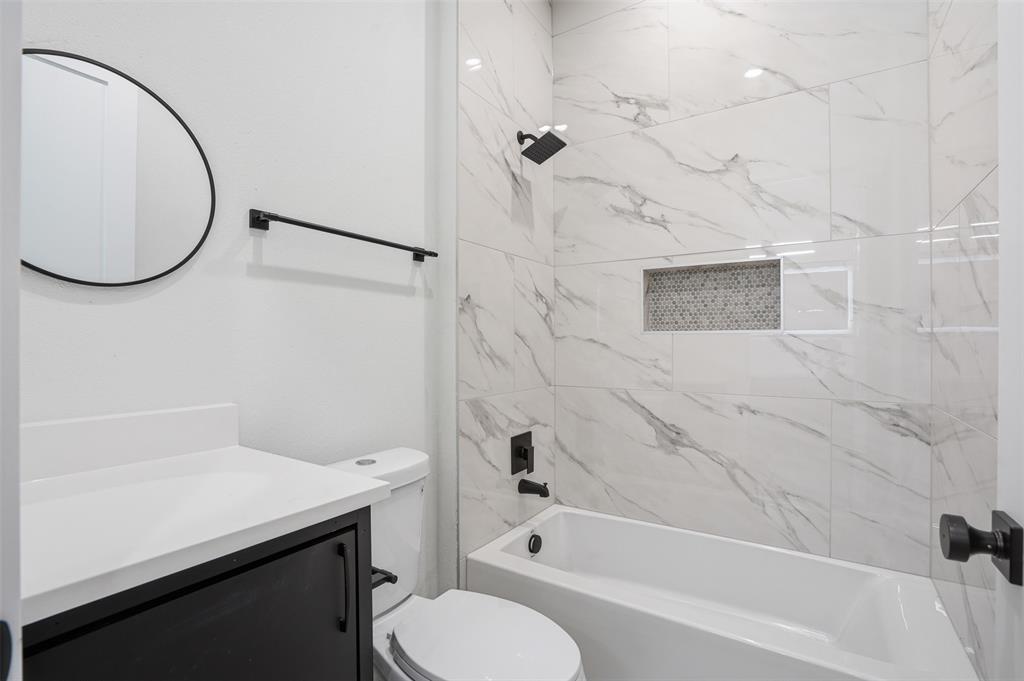 1111 Riverwood Road Dallas, TX 75217 - Photo 31 of 40 Bathroom featuring large format wall tiles, a built-in shower niche with mosaic tile, a dark wood-finish vanity with a white countertop, and matte black fixtures