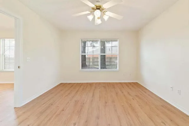 an empty room with wooden floor chandelier fan and windows