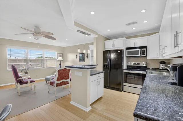 a kitchen with stainless steel appliances kitchen island granite countertop a refrigerator a stove a sink a dining table and chairs with wooden floor