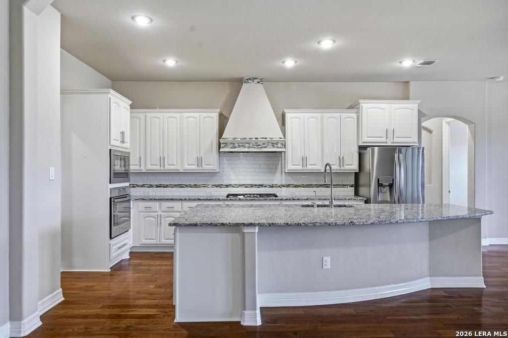 287 Cascade Trail Castroville, TX 78009 - Photo 12 of 46 a kitchen with stainless steel appliances granite countertop a stove a sink and white cabinets with wooden floors