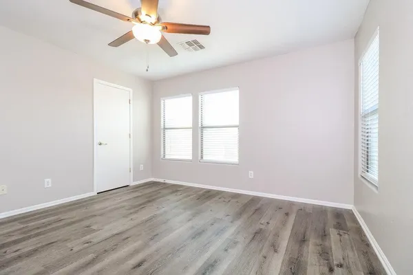 an empty room with wooden floor chandelier fan and windows