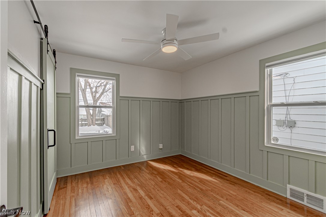 4157 Verona Road Cleveland, OH 44121 - Photo 11 of 26 Unfurnished room with a barn door, light wood finished floors, a wainscoted wall, a ceiling fan, and a decorative wall