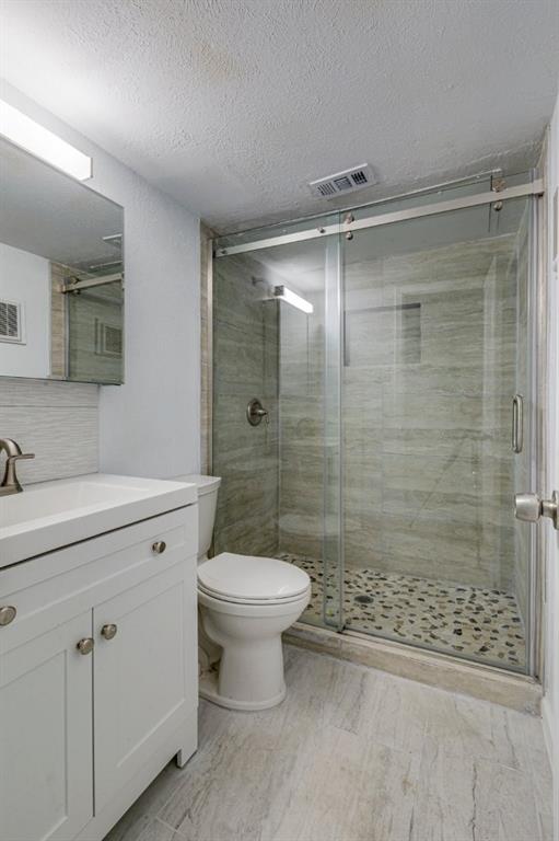 4606 Chaha Road, Unit 106 Garland, TX 75043 - Photo 8 of 22 Bathroom featuring decorative backsplash, vanity, toilet, a shower with door, and a textured ceiling