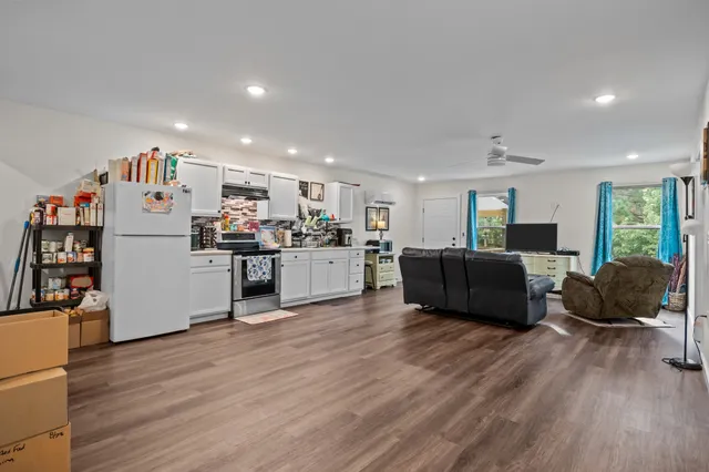 a large white kitchen with stainless steel appliances kitchen island a stove a refrigerator a couch and a dining table with wooden floor