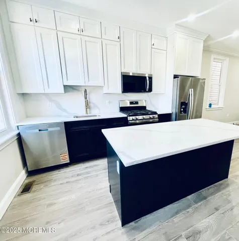 a kitchen with stainless steel appliances a sink a stove a refrigerator a center island and cabinets